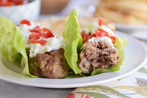 Falafel meatball lettuce wraps topped with red pepper and tzatziki on a white plate.