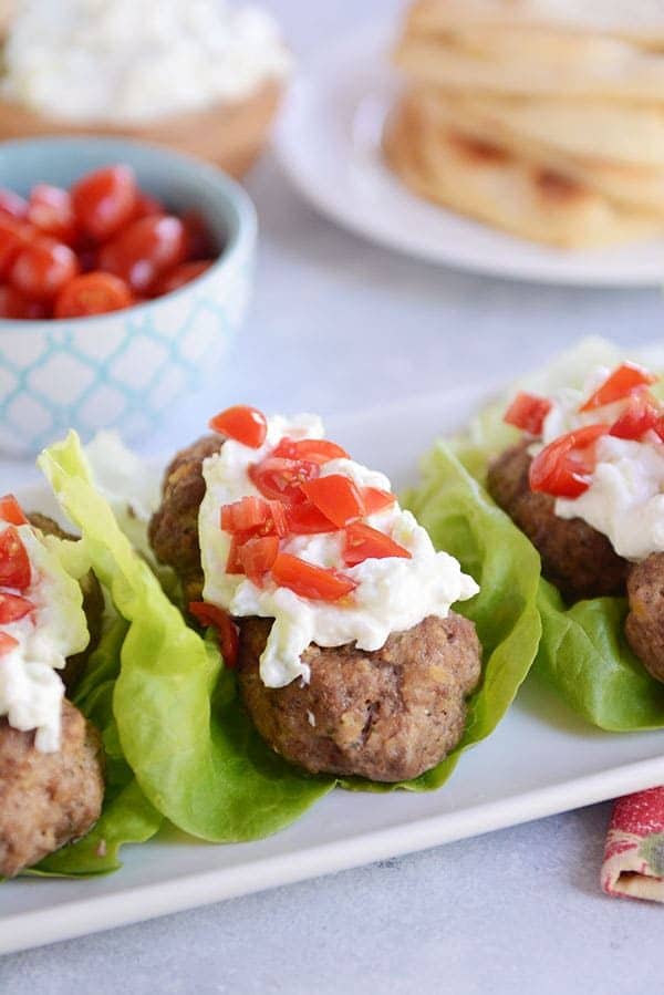 Falafel meatball lettuce wraps topped with tzatziki sauce and chopped peppers on a white platter.