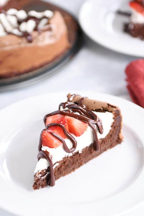 Fallen chocolate cake with whipped cream, strawberries and chocolate ganache on white plate.