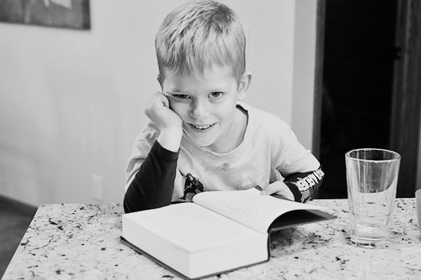 A little boy reading a large chapter book. 