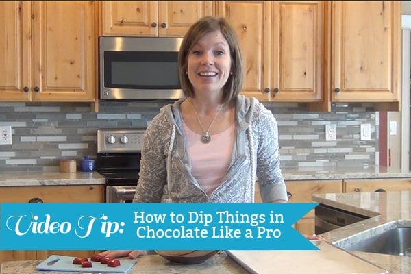 A woman standing in her kitchen dipping caramels in chocolate.