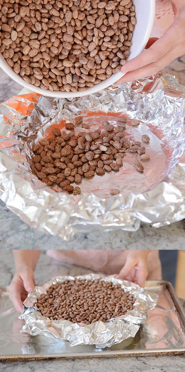 Dry pinto beans getting poured into a tinfoil-lined pie crust.