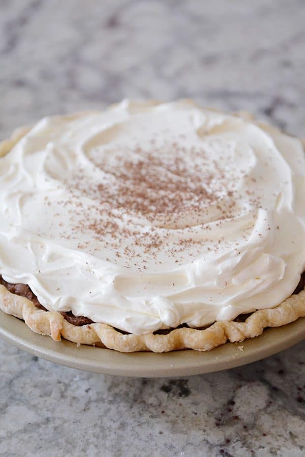 A chocolate ganache pie topped with whipped cream and dusted cocoa powder.
