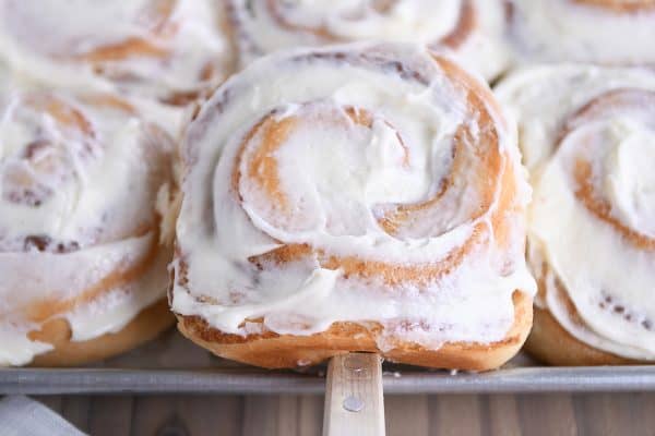 Spatula lifting out frosted cinnamon roll from half sheet pan.