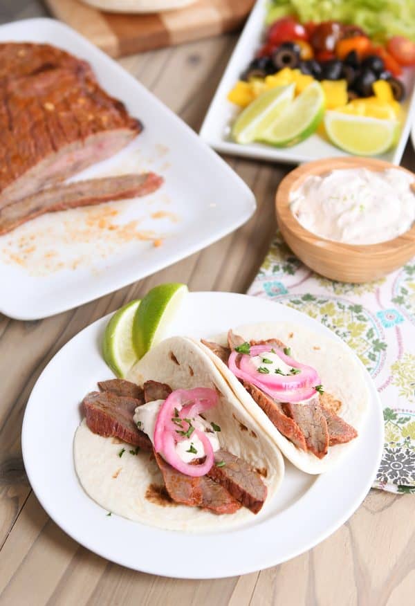 Flank steak fajitas on white plate with tortillas and pickled onion.