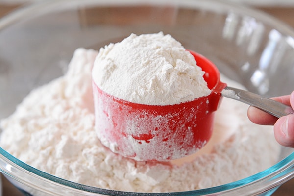 A heaping cupful of flour over a bowl of flour. 