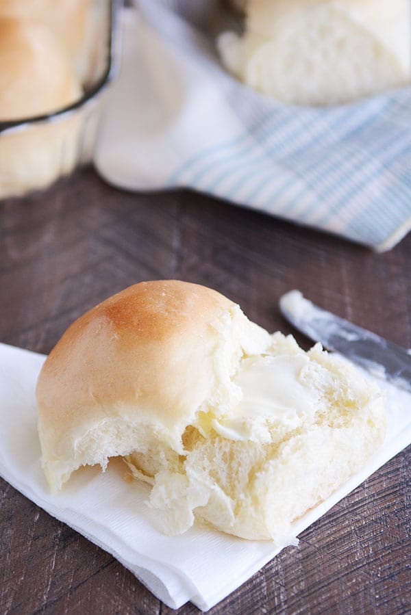 A french bread roll on a white napkin, split in half with butter spread on the inside.