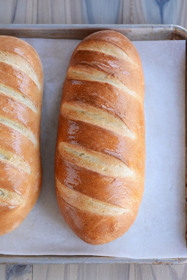 Two loaves of fresh homemade French Bread on a parchment-lined sheet pan.