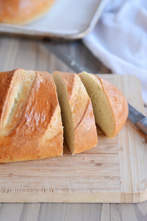 A loaf of french bread on a cutting board with two slices cut out. 