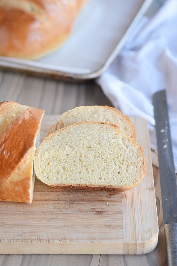 A loaf of french bread on a cutting board with two slices cut out. 