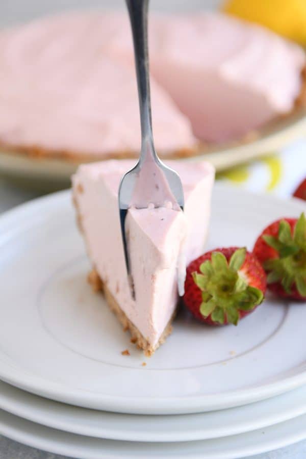 Fork digging into a bite of frozen strawberry lemonade pie on white plate.