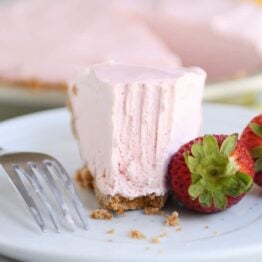 Half eaten slice of frozen strawberry lemonade pie on white plate.