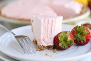 Half eaten slice of frozen strawberry lemonade pie on white plate.