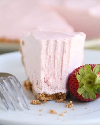 Half eaten slice of frozen strawberry lemonade pie on white plate.