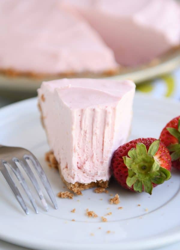 Half eaten slice of frozen strawberry lemonade pie on white plate.