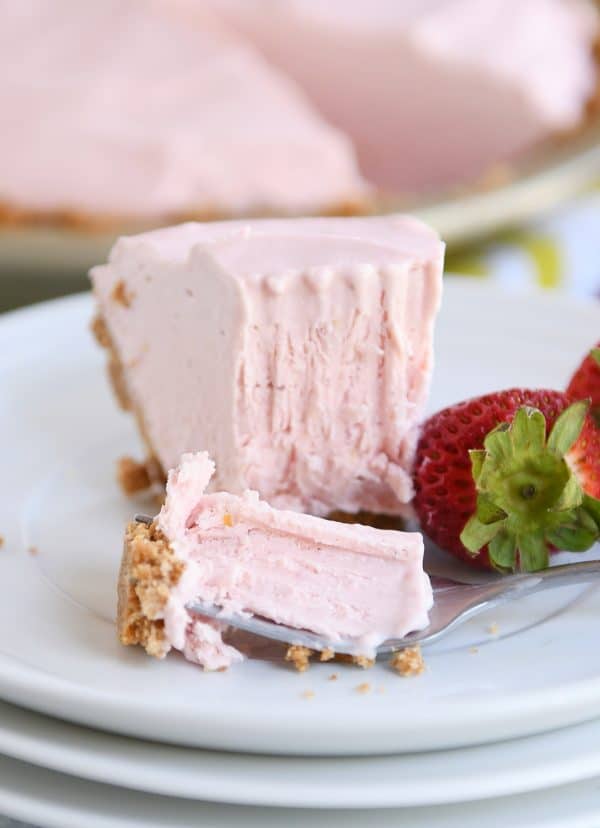 Slice of frozen strawberry lemonade pie with bite taken out on white plate.