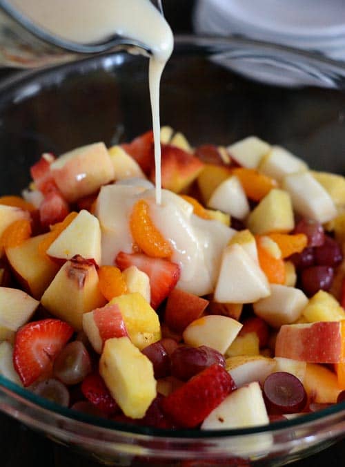 A bowl of fruit salad getting glaze poured over the top. 