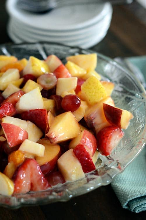 A glass bowl of fruit salad covered in a light glaze. 