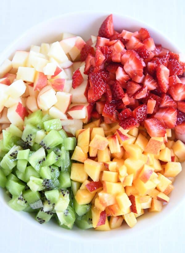 White bowl with diced apples, kiwis, peaches and strawberries.