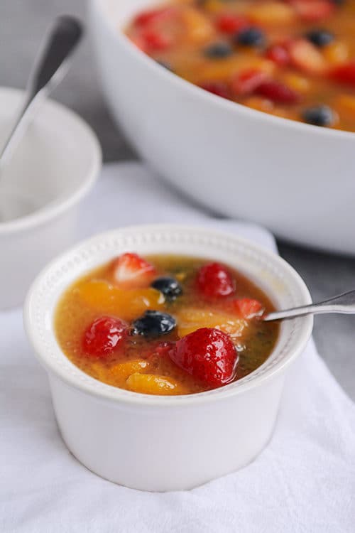 A small white bowl full of fruit soup with a spoon inside.