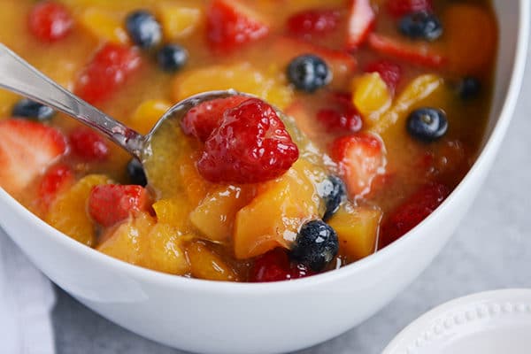 Top view of a white bowl with a spoon taking a bite of fruit soup out of it.