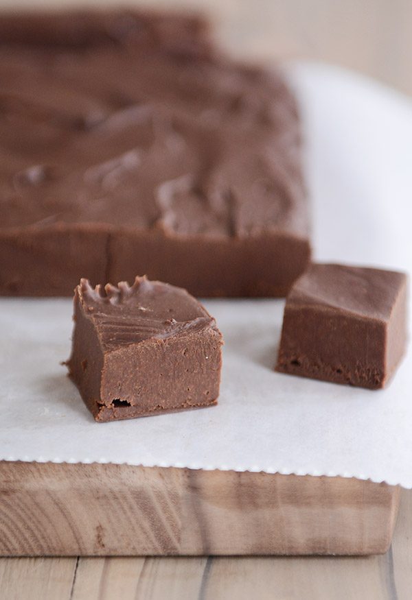 A brick of fudge with two squares of it cut out and placed in front, all on parchment paper. 