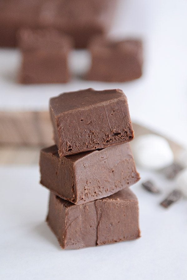 Three cubes of fudge stacked on top of each other, with more cubes in the background. 