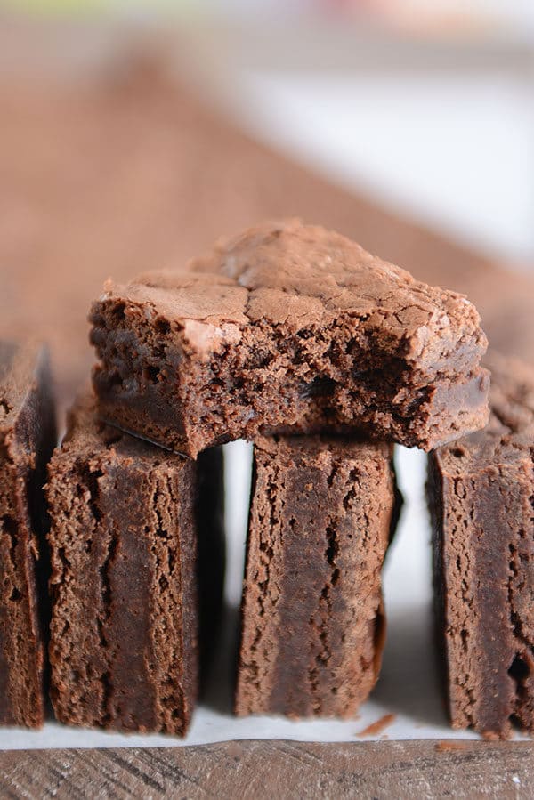 Three brownies stacked on their sides with another brownie with a bite taken out on top.