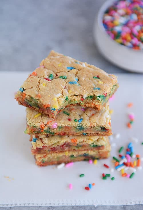 Funfetti blondie bars stacked on top of each other with the top bar with a bite taken out.