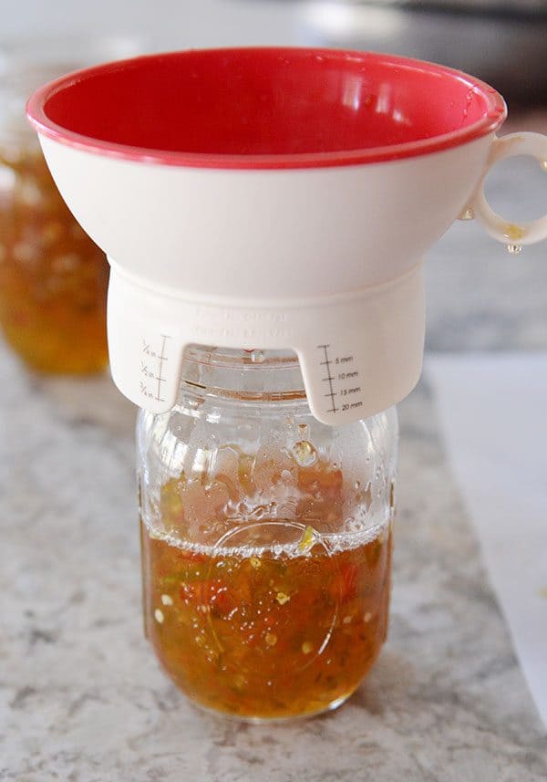 A plastic funnel sitting on top of a half-full mason jar of pepper jelly. 