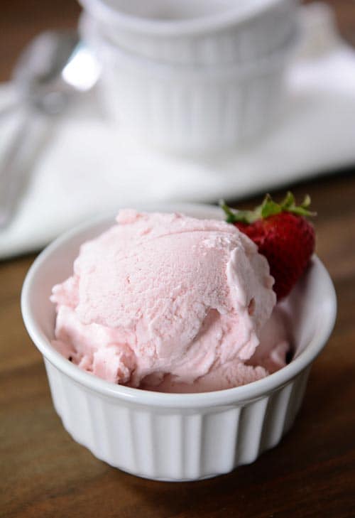 A white ramekin full of scoops of fresh strawberry gelato with a strawberry on the side. 