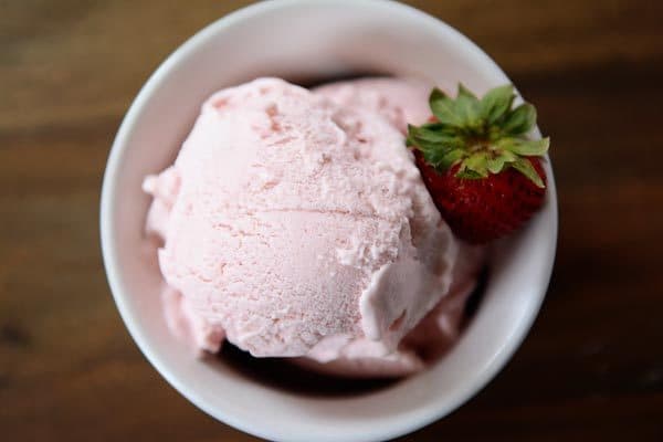 Top view of a white bowl full of fresh strawberry gelato with a strawberry on the side. 