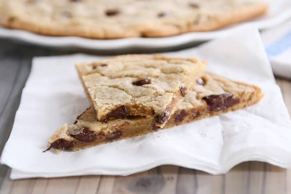 Giant chocolate chip cookie in slices on white napkin.