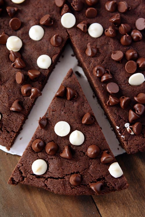 A pie shaped piece cut out of a giant chocolate chip studded chocolate cookie.