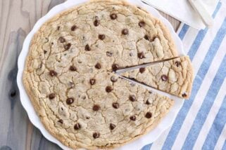 Giant chocolate chip cookie on white platter with slice cut.