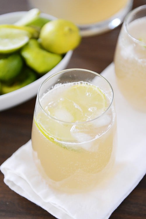 Top view of two glasses of iced limeade in front of a white bowl of sliced limes.