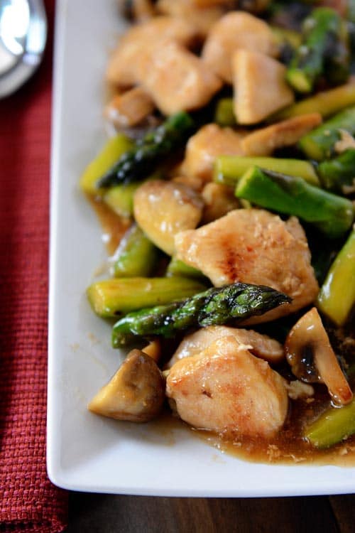 A long white platter filled with chicken and asparagus stir fry covered in sauce. 
