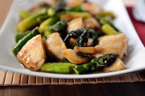 A white rectangular platter full of chicken and asparagus stir fry. 