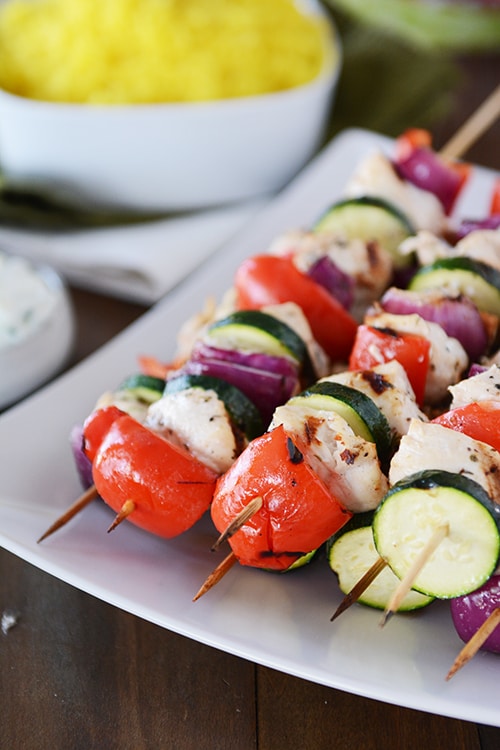 A white platter with grilled chicken and vegetable Greek kebabs. 