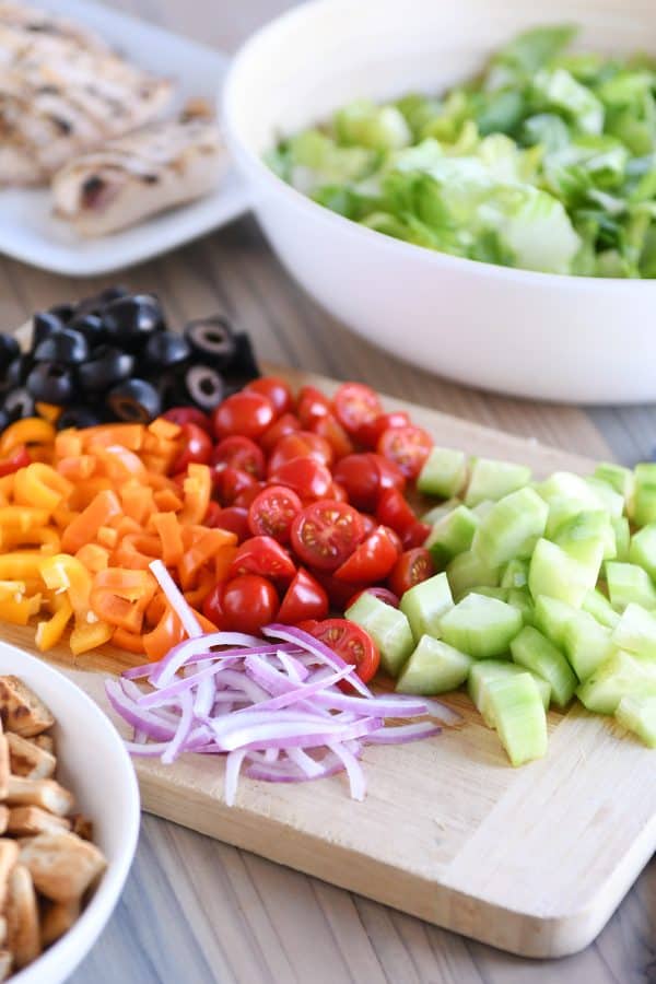 Wood cutting board with chopped cucumbers, tomatoes, peppers and olives.