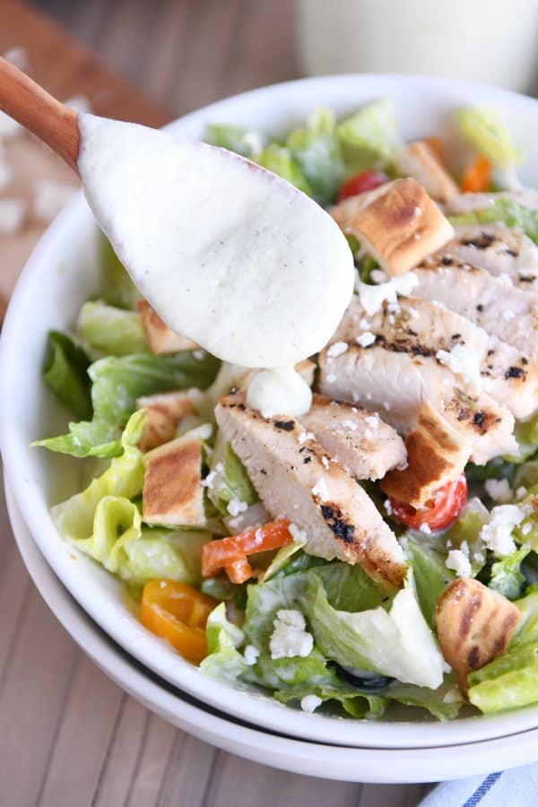 Drizzling tzatziki dressing over chopped Greek chicken salad.