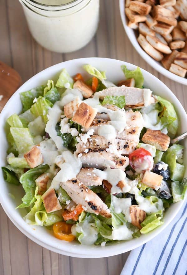 Top down view of chopped Greek salad in white bowl with tzatziki dressing.