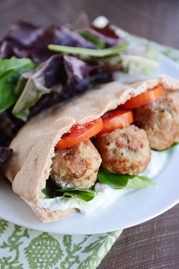 A meatball and veggie stuffed Greek pita next to a large serving of lettuce on a white plate.