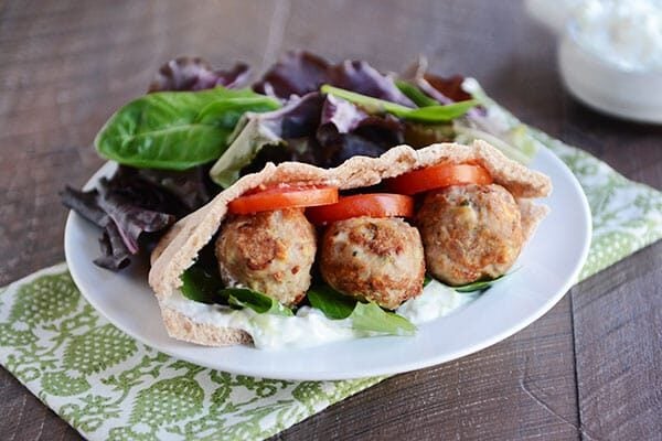  A meatball and veggie stuffed Greek pita next to a pile of lettuce.