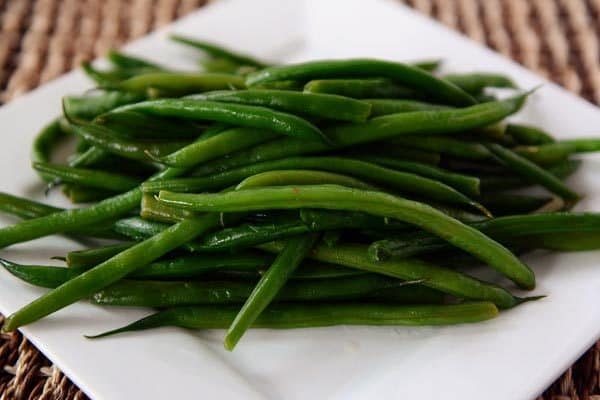 A white platter with a large serving of cooked green beans. 
