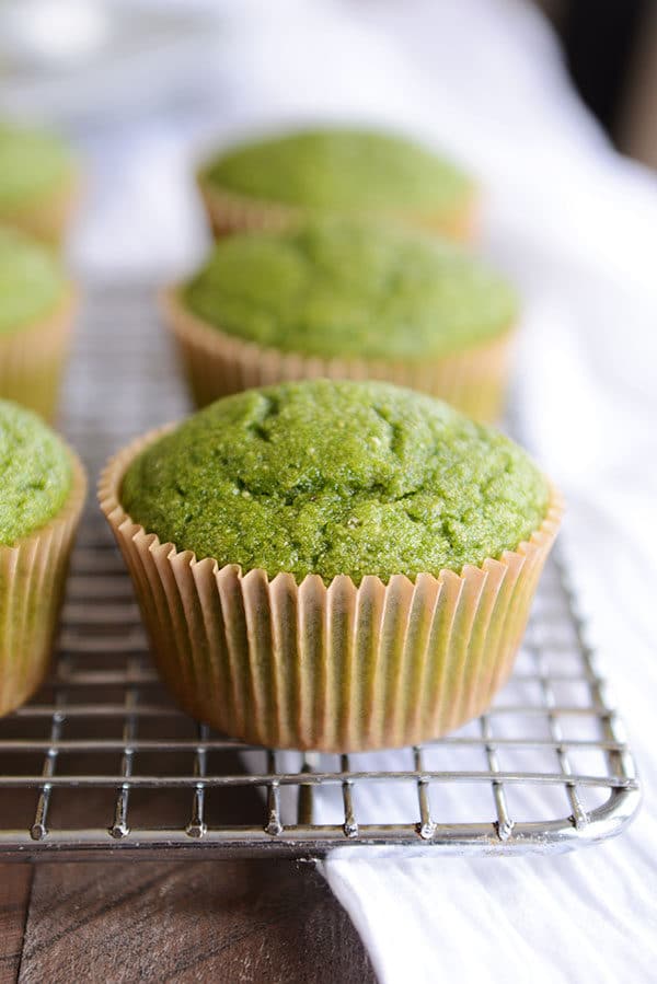 Green muffins in brown muffin liners on a cooling rack.