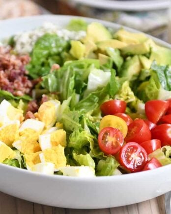 Grilled chicken cobb salad in white bowl with lettuce, tomatoes, eggs, bacon and blue cheese.