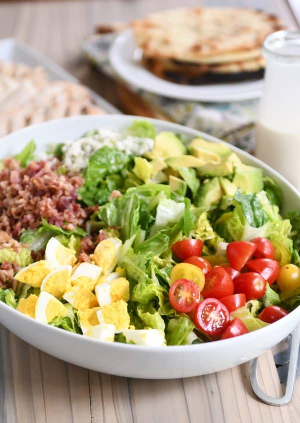 Grilled chicken cobb salad in white bowl with lettuce, tomatoes, eggs, bacon and blue cheese.