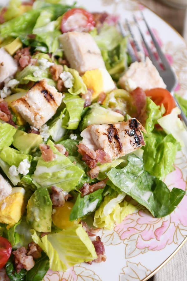Grilled chicken cobb salad on white plate with pink flowers.