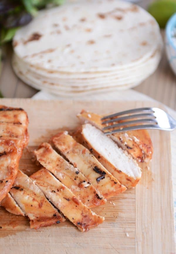 Grilled chipotle chicken sliced into pieces on wood cutting board.